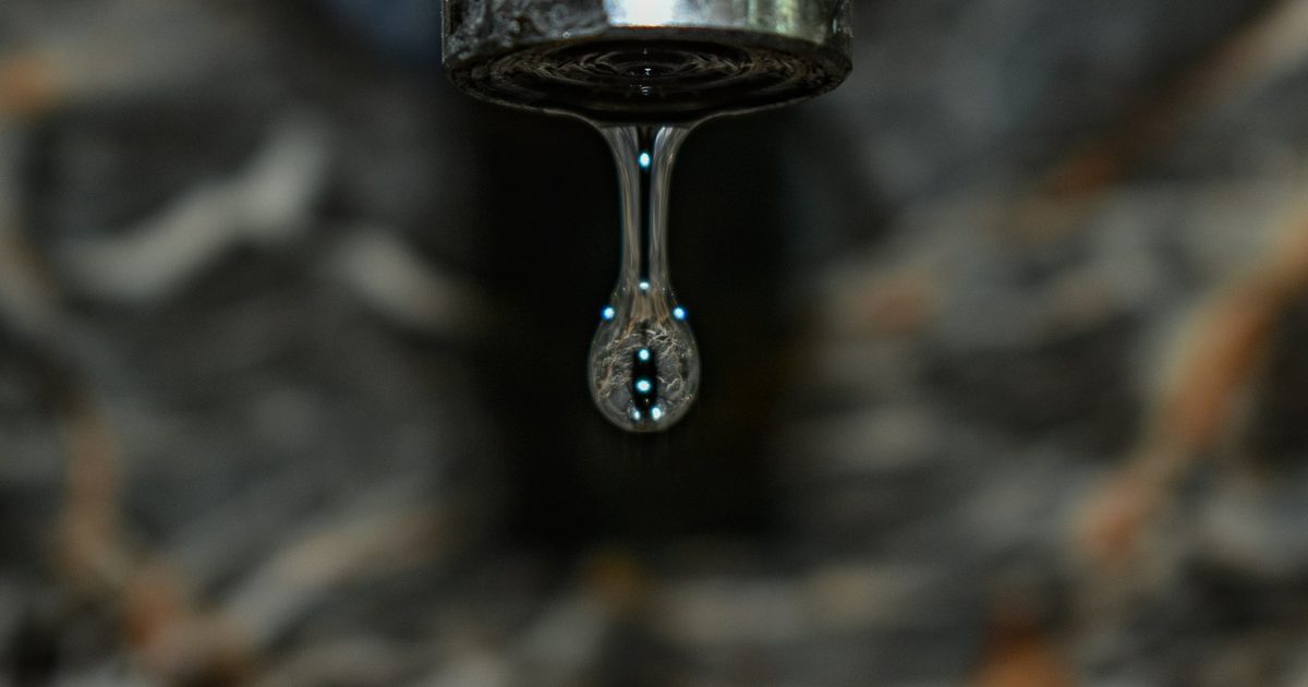 A water drop forming on the end of a tap in the dark