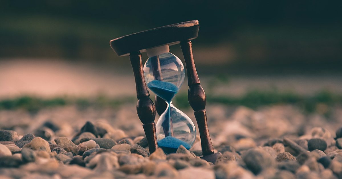An hourglass standing on a bed of stones with the sand part-run