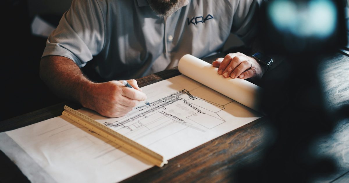 A designer drafting a plan on paper with a pencil and ruler