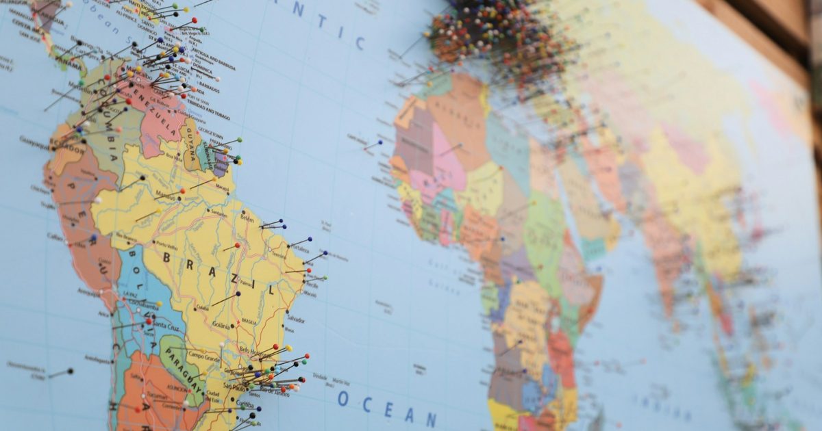 A printed world map with coloured pins marking locations across several continents