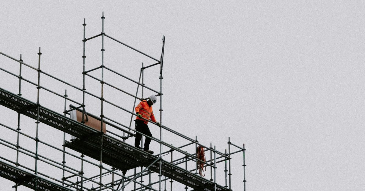 A worker standing on scaffolding erected against a building under renovation