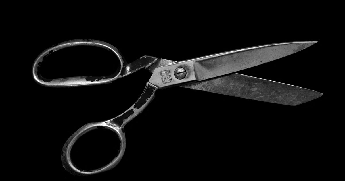 A pair of open steel scissors photographed against a black background